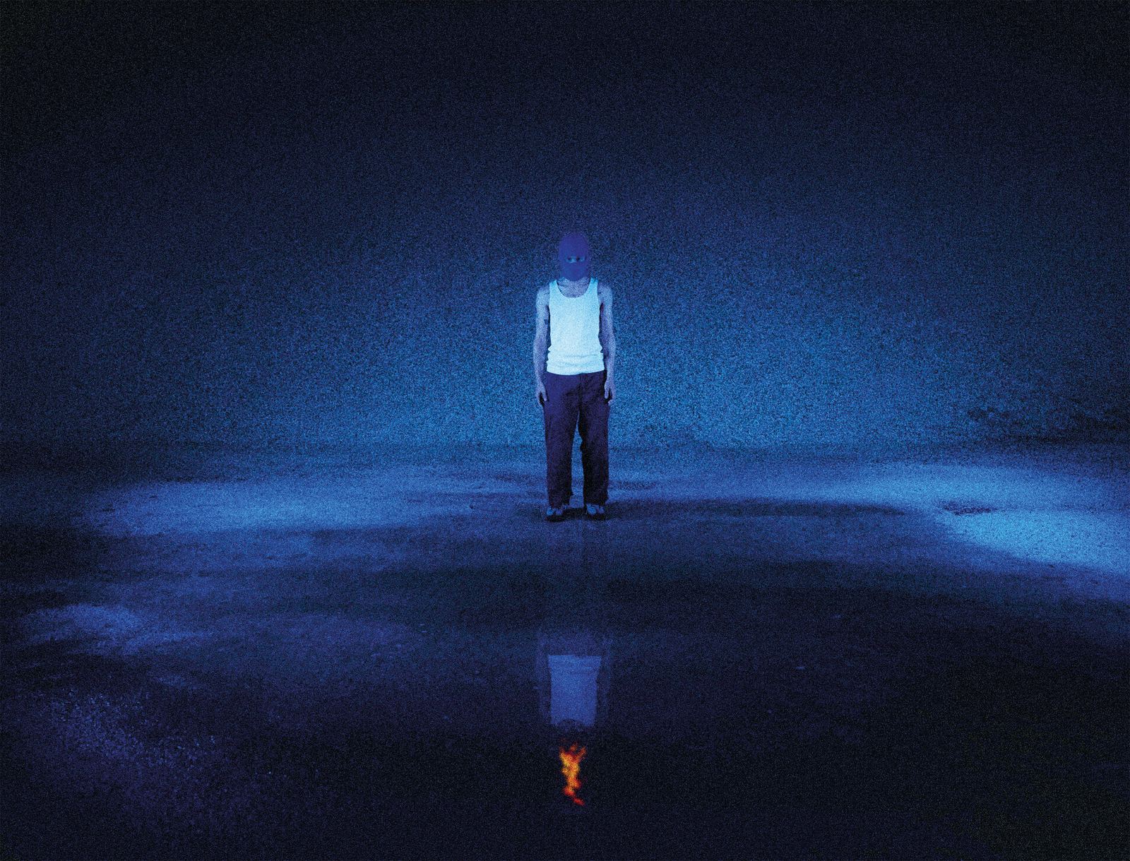 Silhouette cagoulée en lumière bleue, reflétée dans une flaque