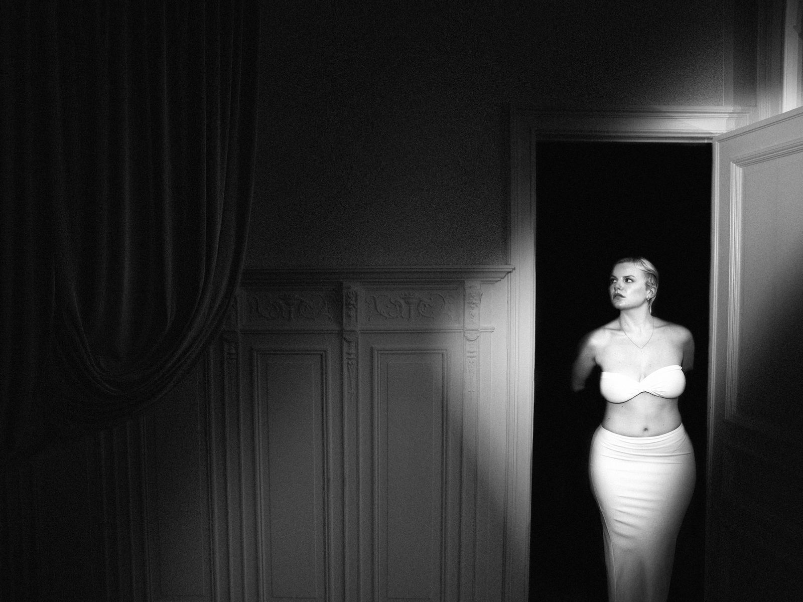 Femme dans l'encadrement d'une porte, dans une pièce sombre, en noir et blanc