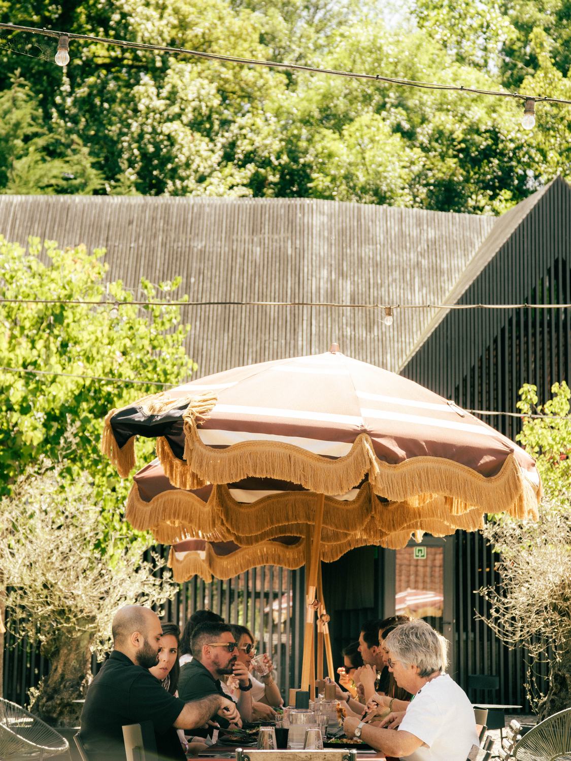 Convives attablés sous des parasols à franges, au soleil