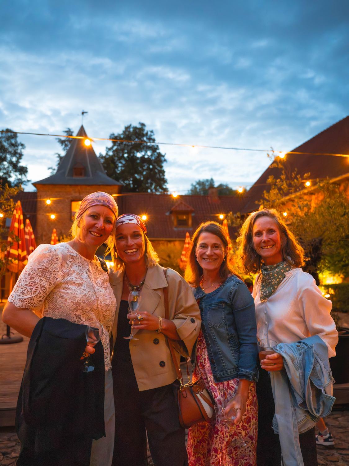 Quatre invitées souriantes au crépuscule, un verre à la main
