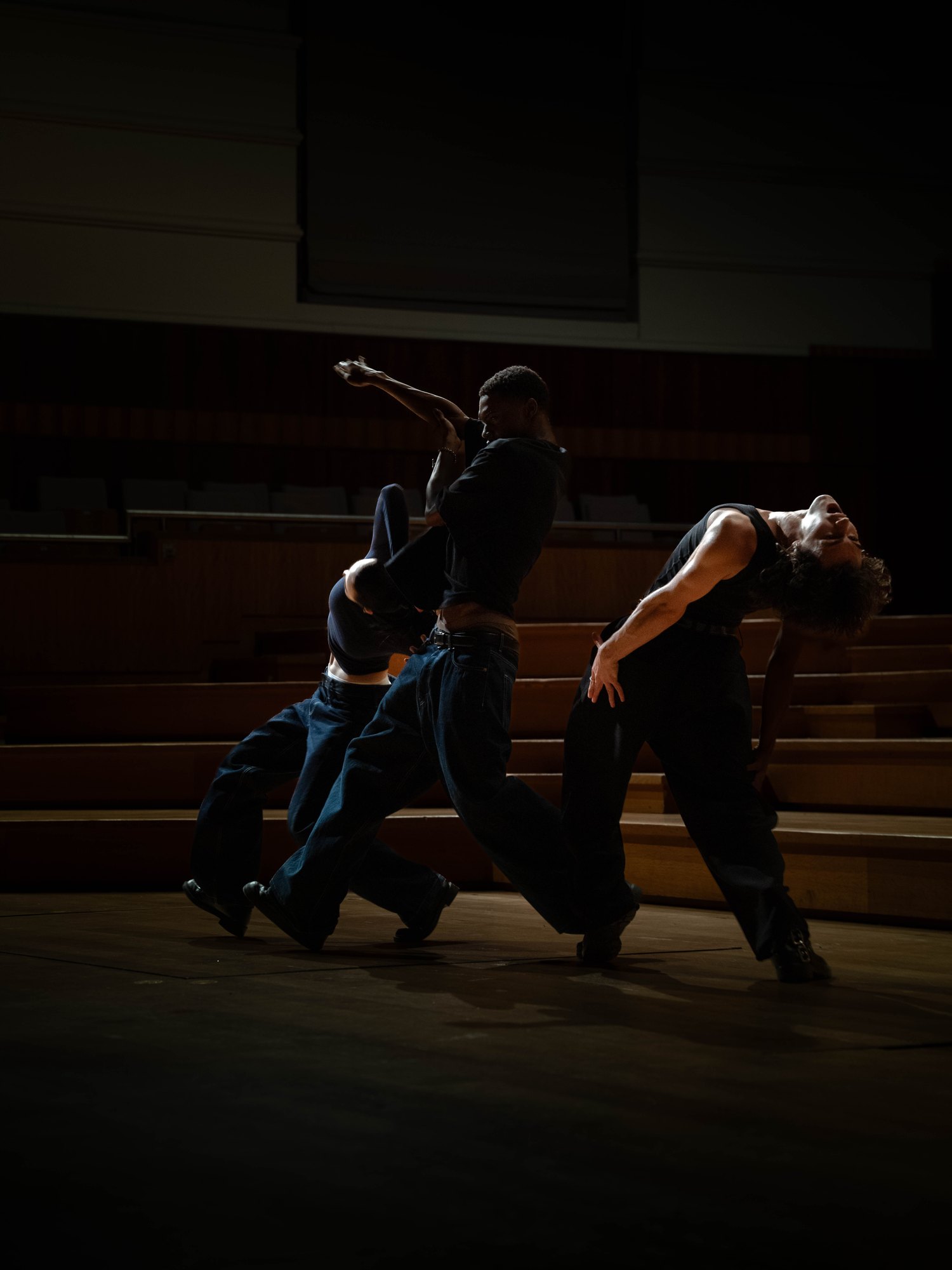 Trois danseurs en mouvement sur scène, dans la lumière