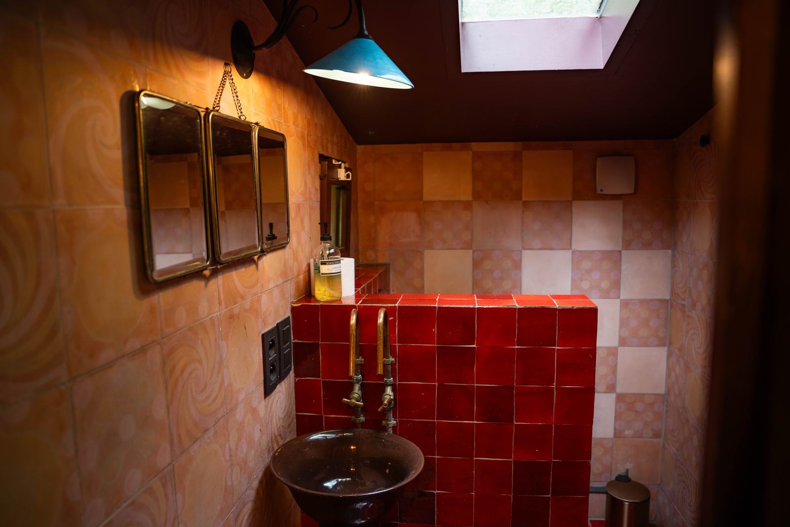 Salle d'eau au carrelage rouge et à la robinetterie en laiton