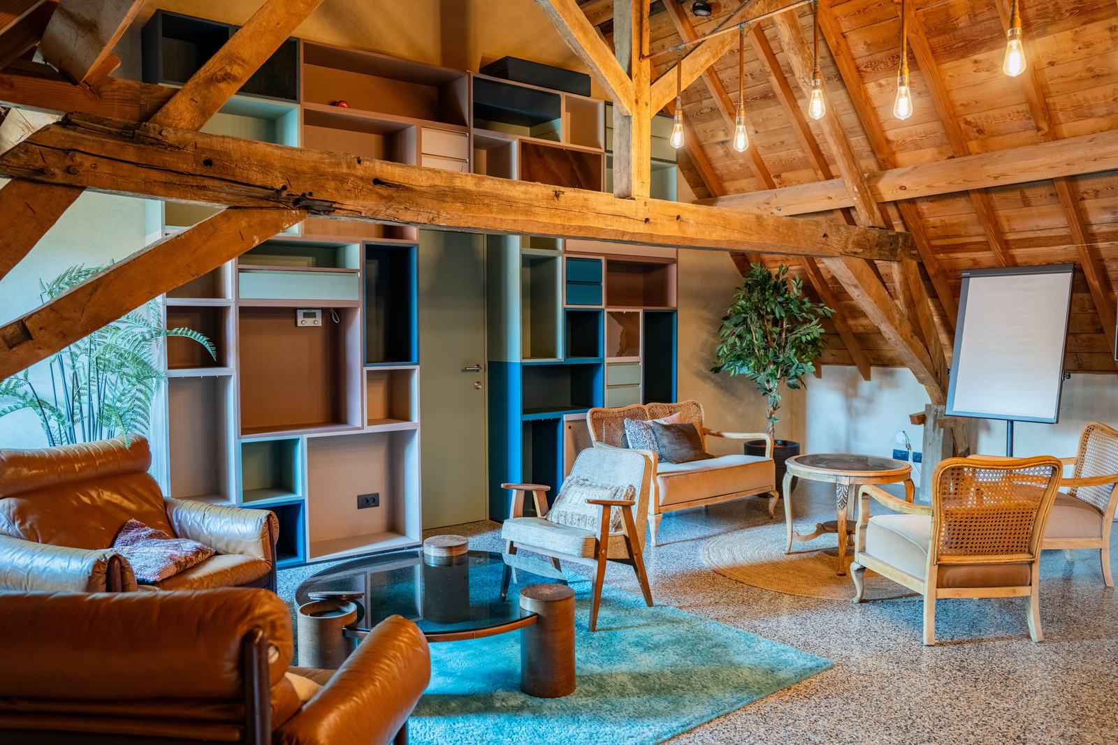 Grande pièce sous charpente avec fauteuils en cuir et bibliothèque colorée