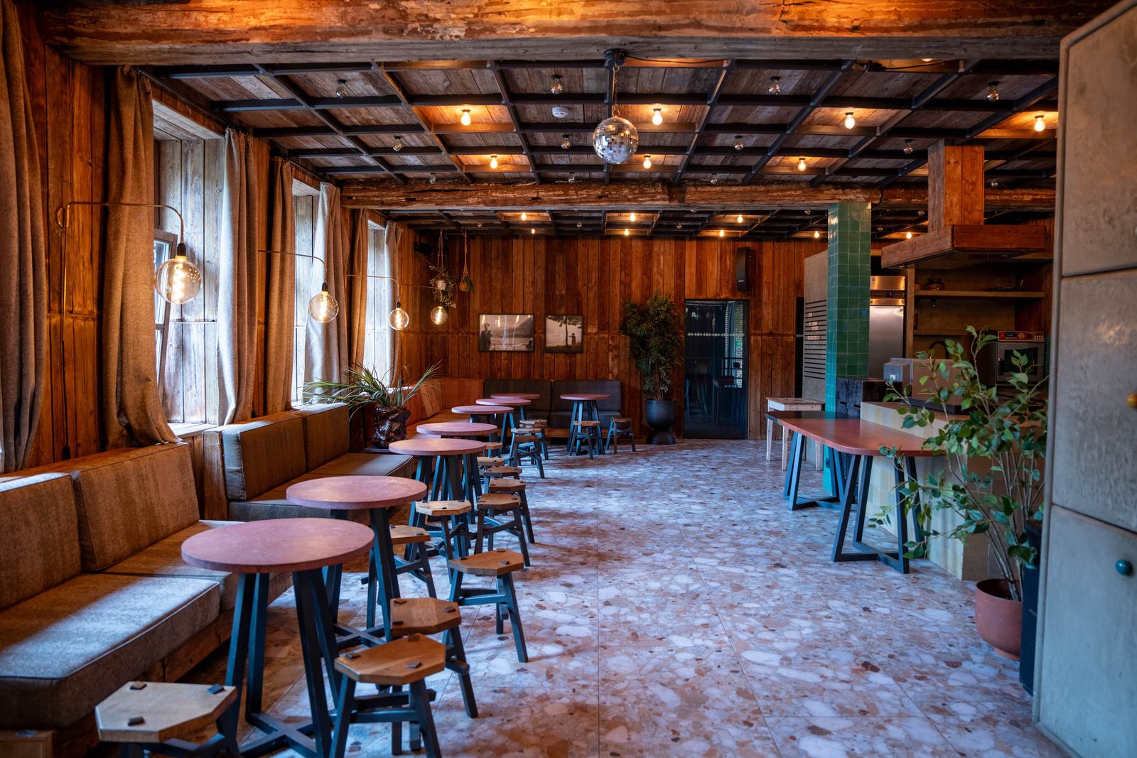 Salle conviviale en bois avec tables hautes rondes et sol en terrazzo