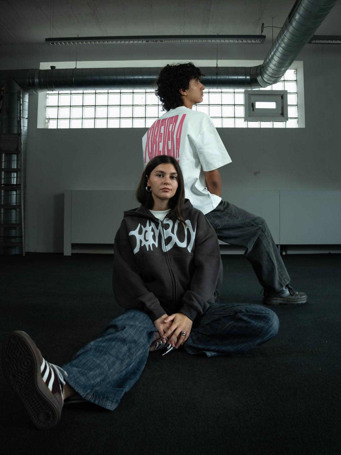 Une modèle assise en sweat zippé Joyboy, un modèle debout de dos
